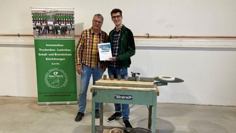 公司创始人 Klaus Papcke 和他的儿子 Phil 正在展示获奖的台式封边机 T-50，这是 1978 年生产的 BRANDT 机型